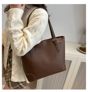 Detail van donkerbruine leren tote bag met witte stiksels en een gouden gesp