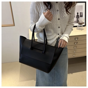 Minimalist black tote bag with dual long handles shown in an elegant lifestyle setting