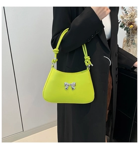 Détail d'un sac à bandoulière vert néon avec nœud argenté et anse nouée sur un costume noir