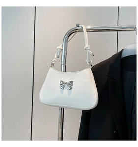 Détail d'un sac baguette blanc avec un nœud argenté et une bandoulière à nœuds
