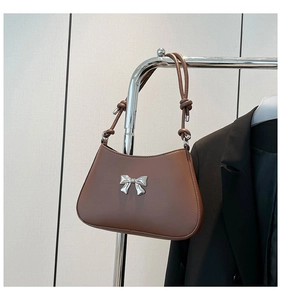 Détail d'un sac marron avec une boucle en métal argenté et des bretelles à nœuds