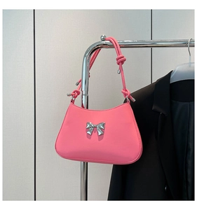 Détail d'un sac porté épaule rose avec nœud et bandoulière nouée sur support métal