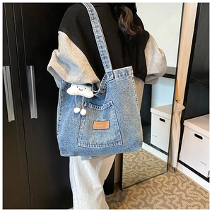 Detail van blauwe denim draagtas met leren logo en witte wolkenhanger als accessoire