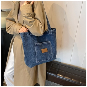 Blauwe denim shopper met leren patch gedragen door model in een stijlvolle trenchcoat