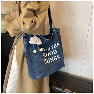 Detail van de blauwe denim draagtas met pluche wolk hanger en witte tekstprint