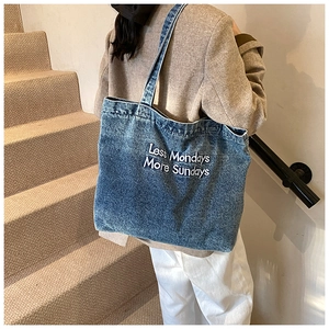 Detail van de grote blauwe denim tote tas met Less Mondays More Sundays borduursel