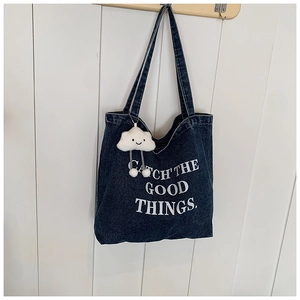 Detail van blauwe denim draagtas met witte tekst en pluche wolk-sleutelhanger