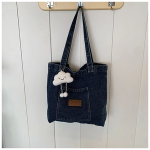 Detailweergave van de donkerblauwe denim tas met leren patch en witte pluchen wolkenhanger