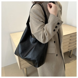 Detail of minimalist black faux leather tote bag with wide strap on wool coat background