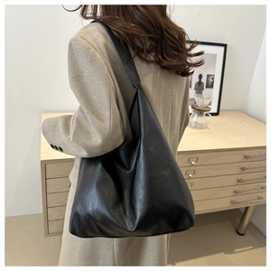 Close-up of minimalist black PU leather tote bag worn on shoulder in home setting