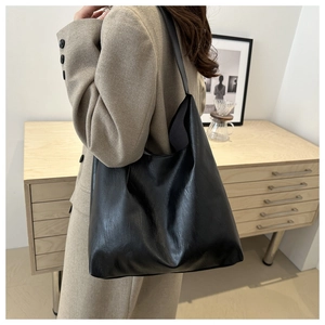 Detail of minimalist black leather tote bag with subtle texture on a female shoulder