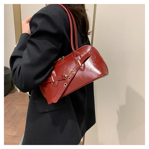 Vue latérale du sac à bandoulière en cuir verni bordeaux porté sur un blazer noir