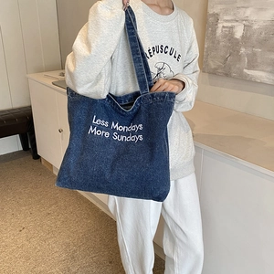 Grote marineblauwe denim shopper met borduursel gedragen door model in een interieur