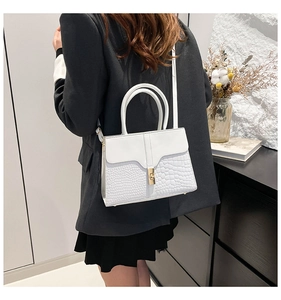 Detail of white crocodile embossed crossbody bag with golden twist lock and twin handles