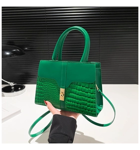 Close-up of green crocodile-pattern crossbody bag with gold square metallic lock detail