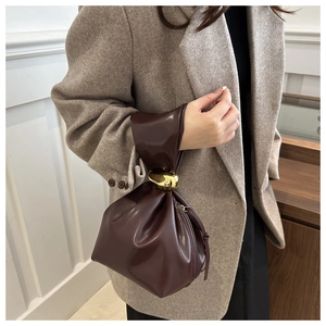 Détail d'un sac seau plissé marron foncé avec une grande poignée en nœud doré et brillant