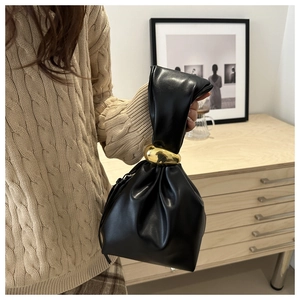 Détail du sac seau en cuir plissé noir avec poignée anneau doré mat sur tricot beige