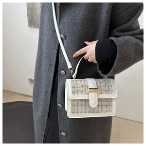 Detail of tweed crossbody bag with golden H clasp and white leather trim on gray coat