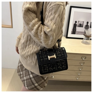 Detail of black tweed crossbody bag with gold buckle on a model in a warm cozy interior