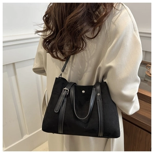 Detail of black tote bag with matte texture and leather straps on model in trench coat