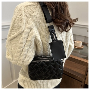 Detail of black crossbody bag with quilted texture and small detachable coin purse on strap