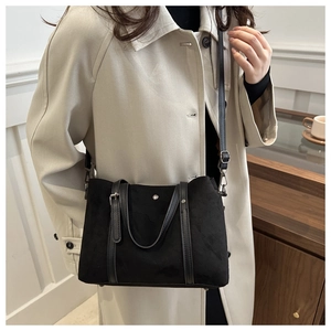 Close-up of matte black tote bag with leather straps on a model wearing a beige coat