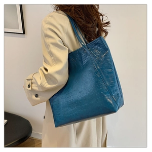 Detailed shot of dark blue crocodile pattern tote bag carried by a model in a trench coat