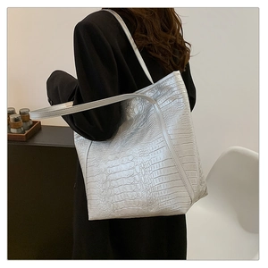 Side view of silver crocodile embossed tote bag worn over the shoulder by a model