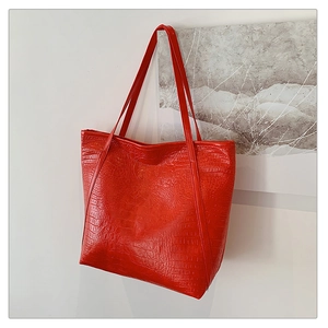 Close-up of a red tote bag featuring crocodile embossed texture and dual shoulder straps
