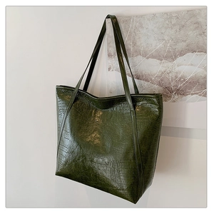 Detail shot of a large dark green tote bag featuring luxury crocodile pattern leather