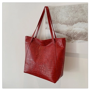 Close-up of red tote bag with crocodile texture and embossed circular logo detail