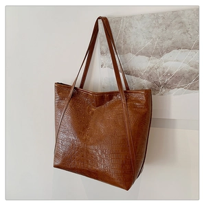 Detailed view of brown crocodile embossed texture and stitching on the tote bag