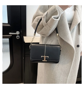 Détail du sac bandoulière en cuir noir avec fermoir en T doré sur manteau beige