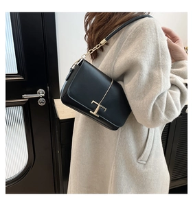 Détail d'un sac bandoulière noir avec boucle dorée en T sur un manteau en laine