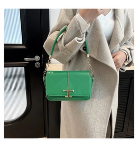 Détail du sac bandoulière vert lime avec fermoir en T doré sur un manteau en laine