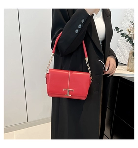 Détail d'un sac bandoulière en cuir rouge avec un fermoir métallique doré en forme de T