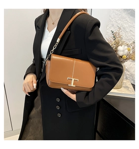 Détail d'un sac bandoulière en cuir marron avec boucle T dorée et bandoulière chaîne