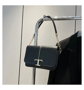 Détail du sac à rabat en cuir noir avec ferrures dorées en T et bandoulière en chaîne