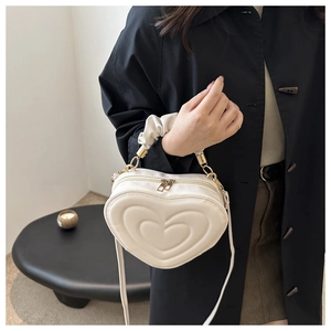 Detail of cream heart-shaped crossbody bag featuring quilted faux leather and gold zippers