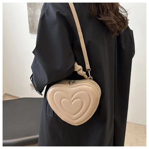 Détail du sac bandoulière beige en forme de cœur avec texture gaufrée sur manteau noir