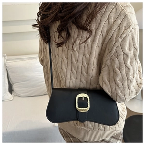 Close-up of black handbag with large gold buckle worn with a beige knitted sweater