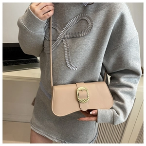 Detail of beige curved shoulder bag with textured gold buckle on a grey sweater