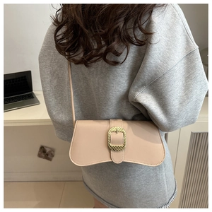Detail of nude wave-shaped crossbody bag with gold textured buckle worn by a model