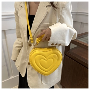 Detail of yellow heart-shaped crossbody bag with quilted texture and pleated handle