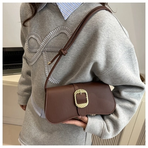 Detail of a dark brown leather baguette bag with a golden geometric textured buckle