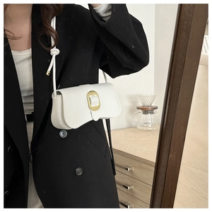 Detail of white baguette bag showing a large golden oval buckle and braided metal texture