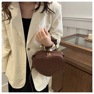 Détail d'un sac à bandoulière en cuir marron foncé en forme de cœur avec poignée plissée dorée