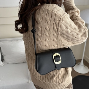 Minimalist black leather underarm bag with gold metal buckle on woman shoulder