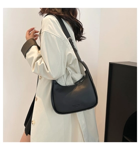 Model wearing a black crescent hobo shoulder bag with adjustable strap and embossed text