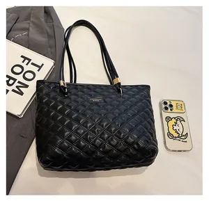 Top view of black quilted tote bag with metal logo and daily essentials for scale
